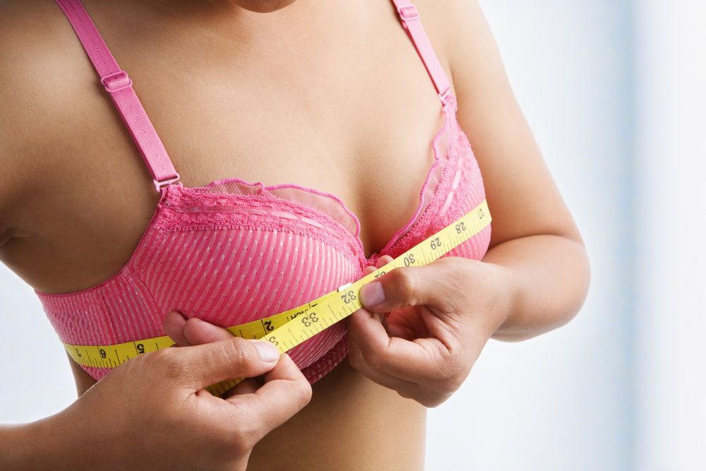 A women using yellow measuring tape to take her bust measurement, while wearing a pink bra.