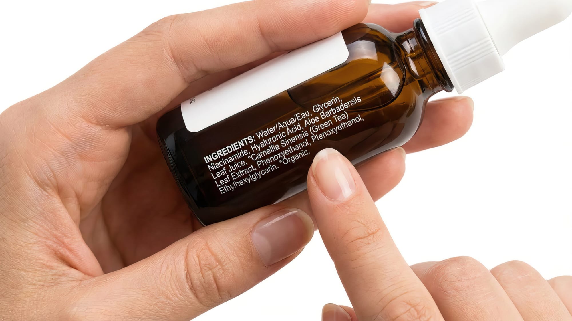 Close-up, overhead shot of hands holding a beauty product bottle, with the ingredient label clearly visible and in focus. 