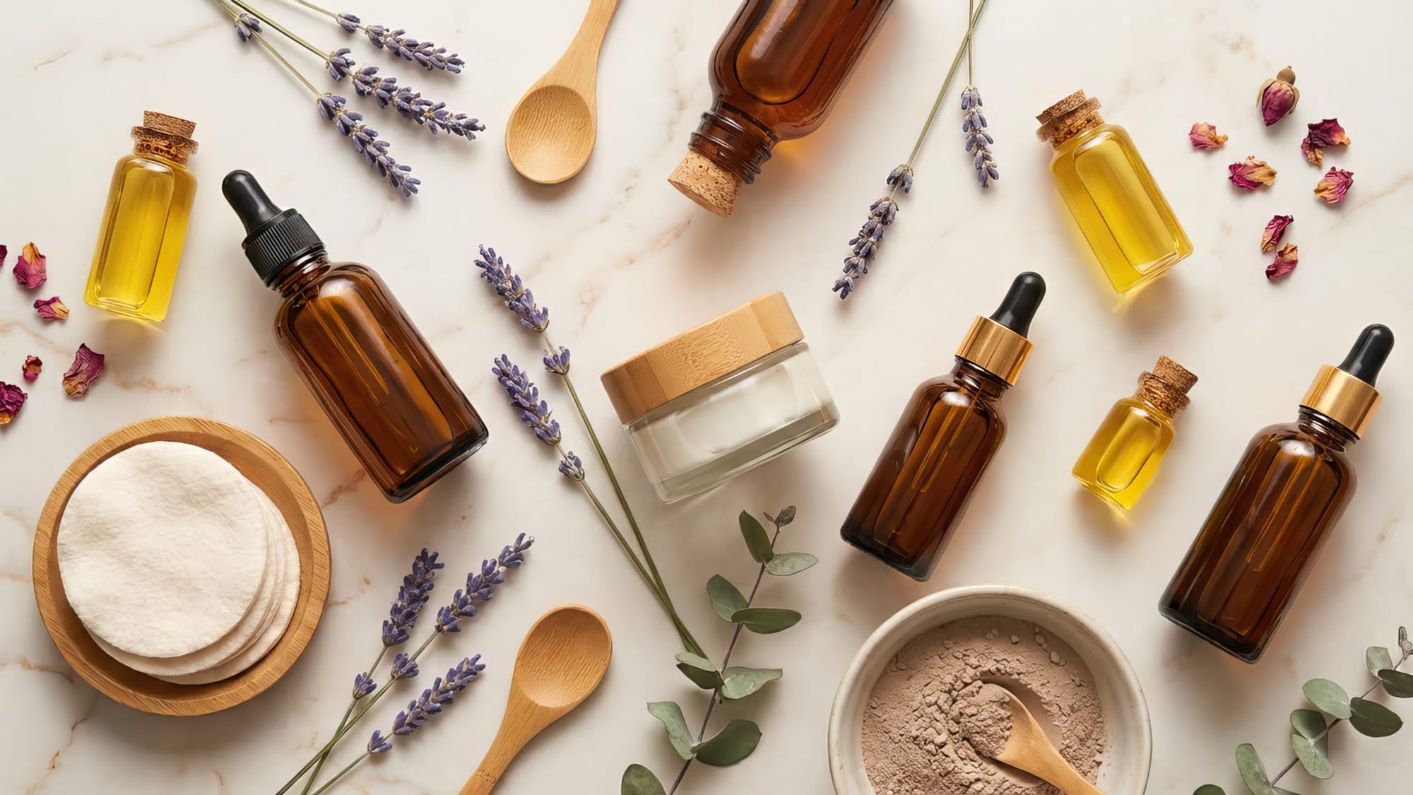 Elegant flat lay of natural facial care products beautifully arranged: glass bottles with natural oils, a jar of cream, fresh botanicals (like lavender or rose petals), natural cotton rounds, all on a marble or light wood surface.